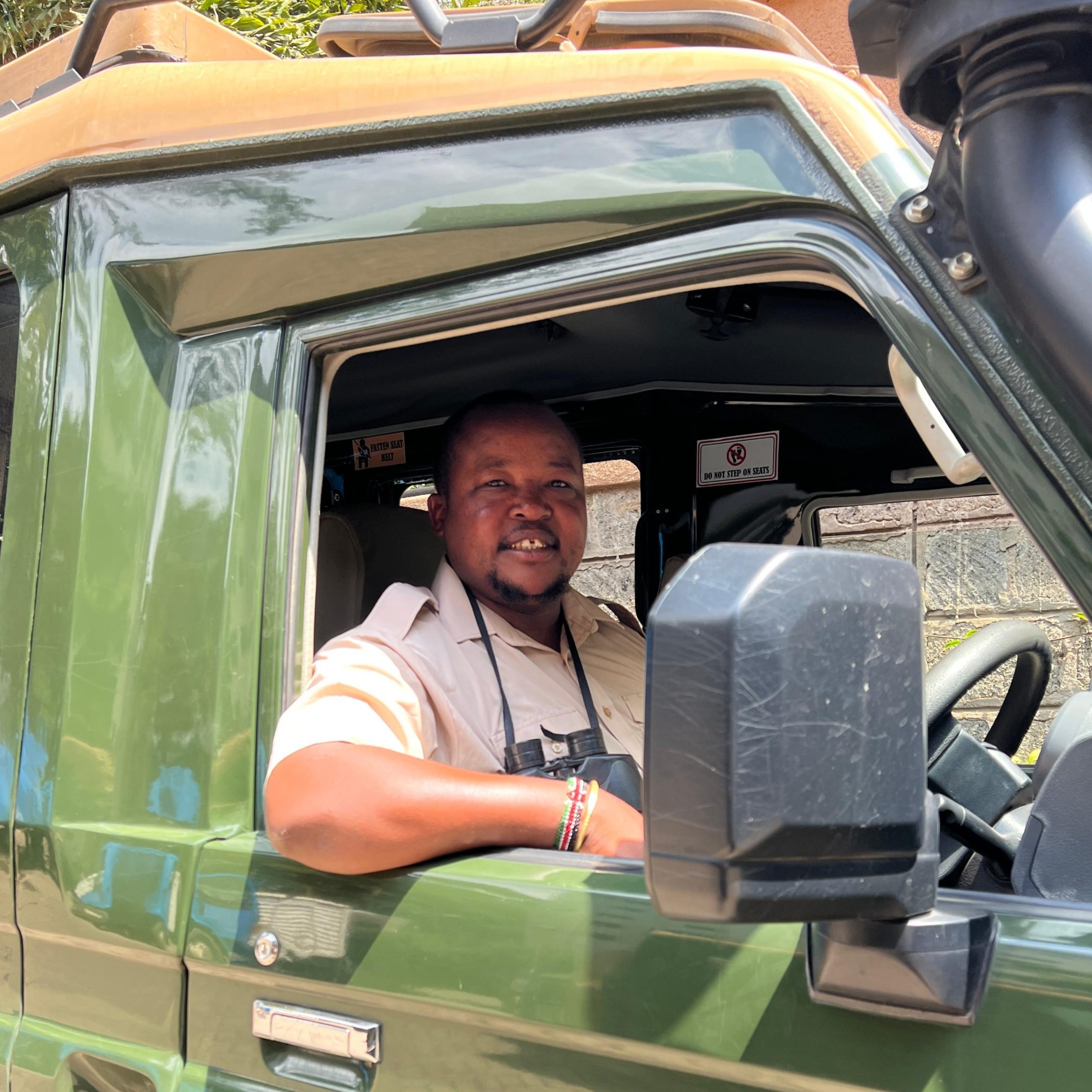 Driver seated in a green pickup with the door open; safety signs visible inside the cabin.