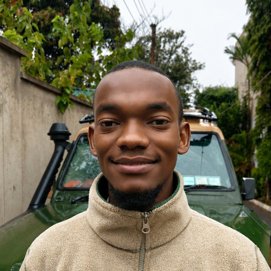 Portrait of a smiling young man in a beige fleece jacket standing in front of a green SUV in a residential driveway.